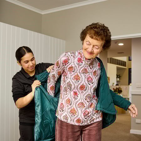 An older woman being helped to put a jacket on by a support worker, as part of independence services.