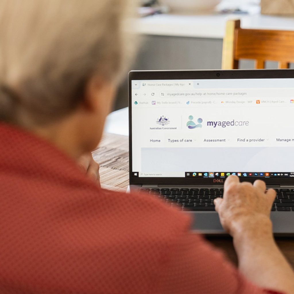 An older woman in red using her laptop to investigate care management services.