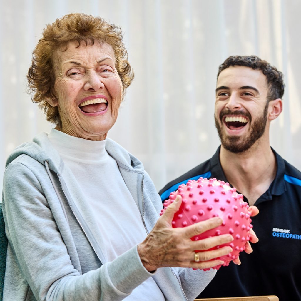A woman laughing with her physio while holding a spiky ball, during s clinical supports session.