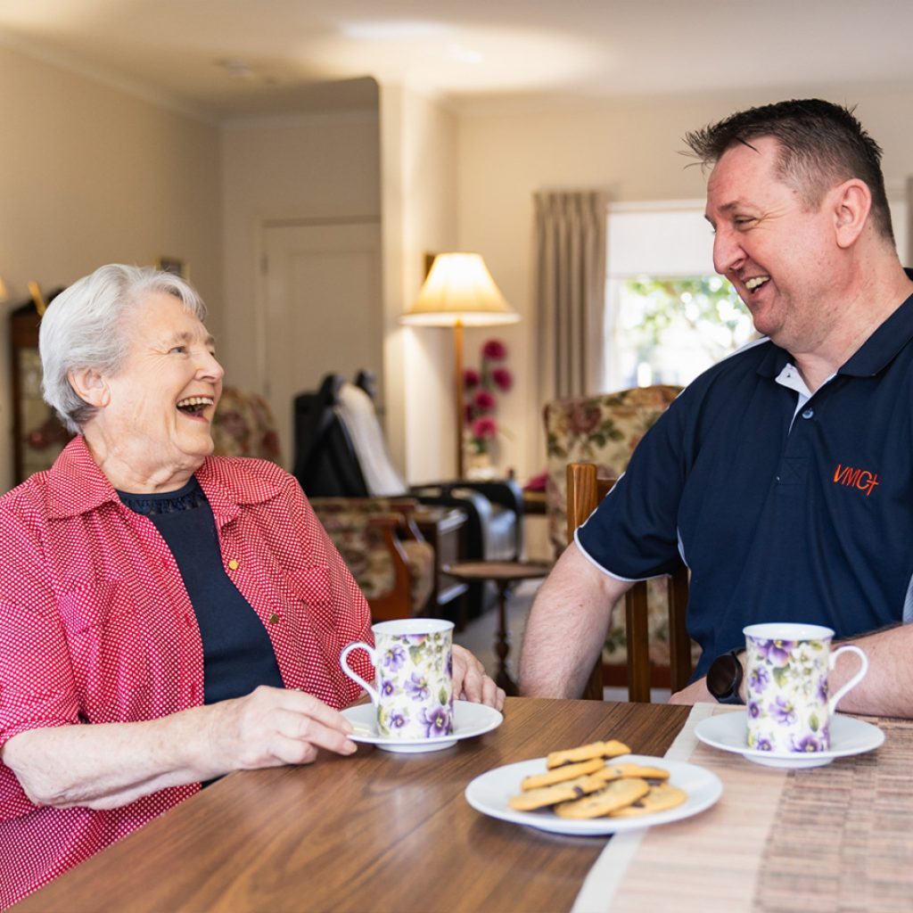 A care partner and his client laughing over a cup of tea while talking about care management services.