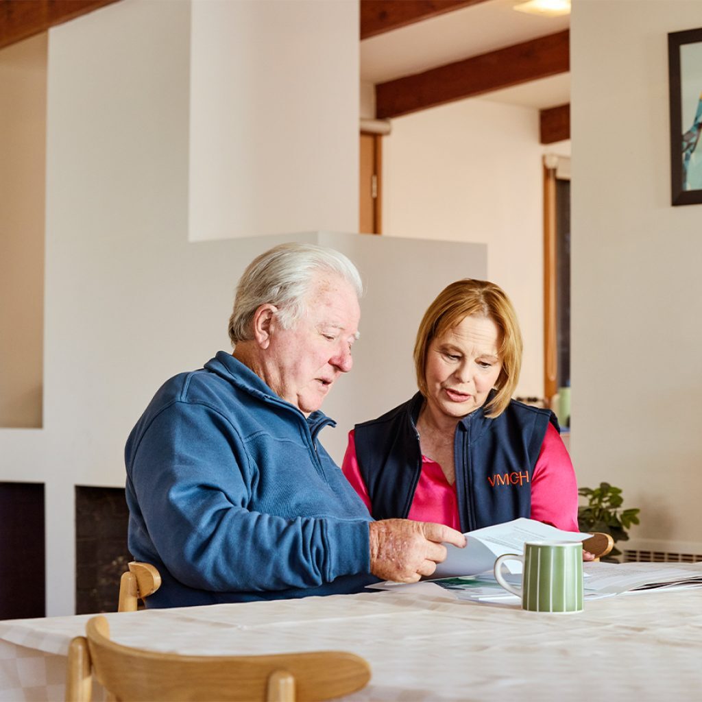 An older man and a support worker sitting at the table looking at paper work.