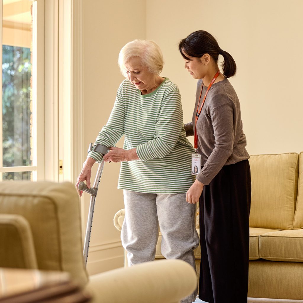 A support worker helping a senior woman use her crutches.