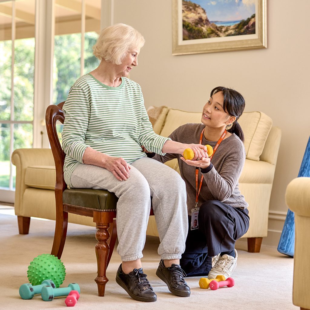 A support worker helping an older woman with her exercises during a clinical supports session.