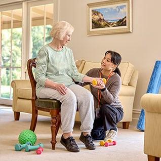 A woman sitting on a chair, while a physio squats next to her