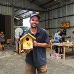 A man holding a bird house in a workshop